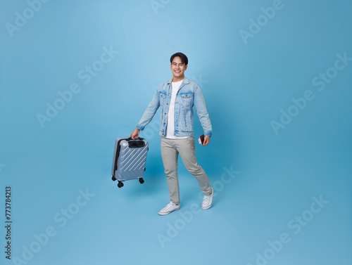 Happy smiling young Asian tourist man holding passport ticket and luggage going to travel on summer holidays isolated on blue background.