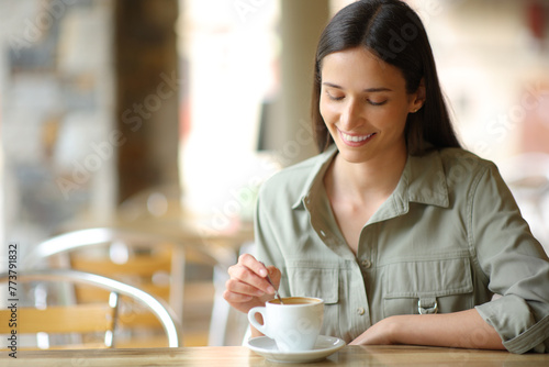 Happy woman in a bar terrace stirring coffee cup