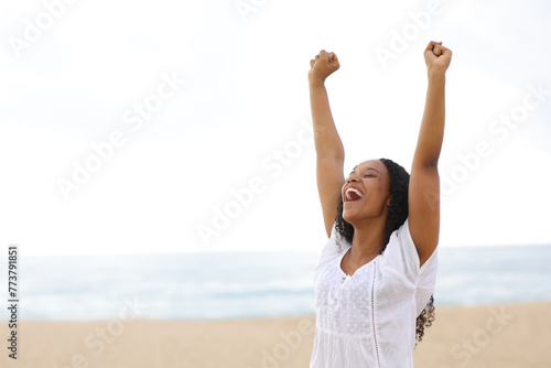Happy black woman raising arms celebrating on the beach