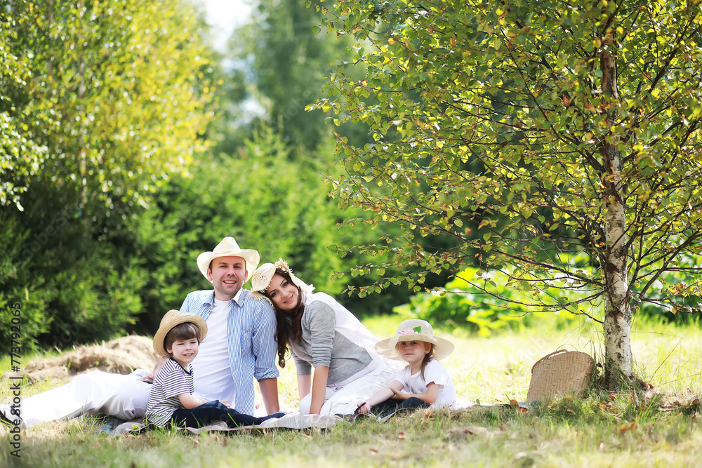 Happy family with children having picnic in park, parents with kids sitting on garden grass and eating watermelon outdoors Happy family with children having picnic in park, parents with kids sitting on garden grass and eating watermelon outdoors