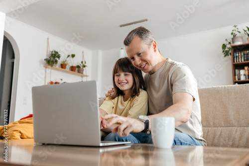 Happy father and daughter watching movie on laptop at home photo