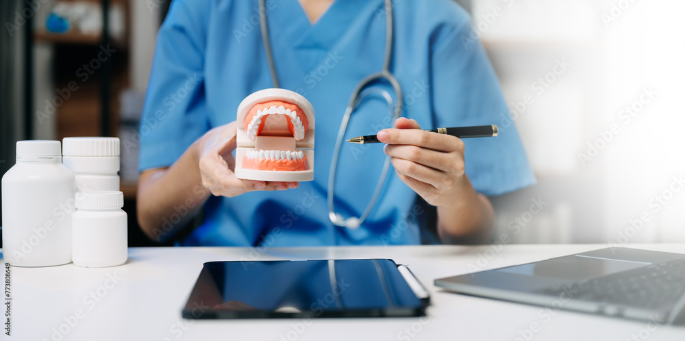 Fototapeta premium Dentist sitting at table with jaw samples tooth model and working with tablet and laptop in dental clinic.