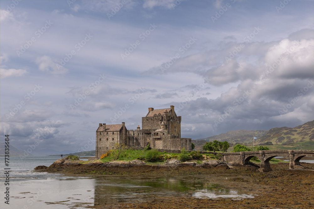Eilean Donan Castle reflects its storied past in the calm loch, flanked by a historic bridge and the undulating hills of the Scottish Highlands