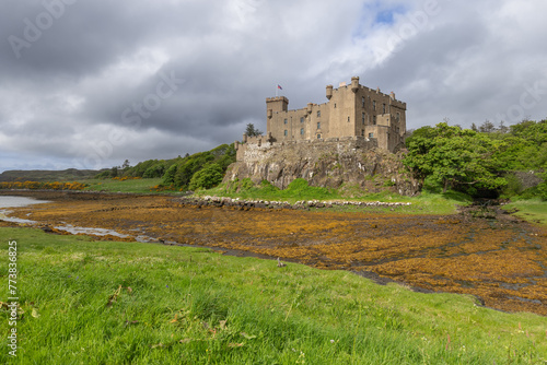 Dunvegan Castle, with its robust stone walls, stands guard over a vibrant, algae-covered shoreline on the Isle of Skye, under a dynamic sky