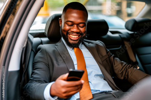 A cheerful businessman in a suit looking at his smartphone inside a car, exuding confidence and happiness © Tixel