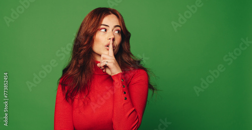 Young woman making shush gesture on a green background