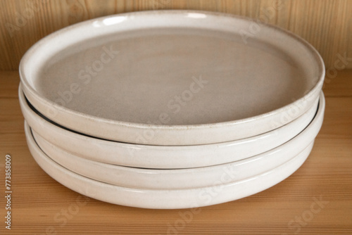 A stack of beige ceramic plates in a wooden cupboard.