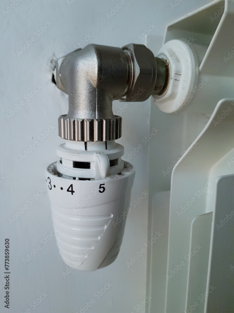 White thermostat on the wall of a white radiator White thermostat on the wall of a white radiator