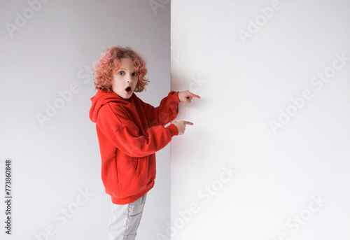 A red-haired boy in a red sweater points his finger at an empty white board, a place for advertising.