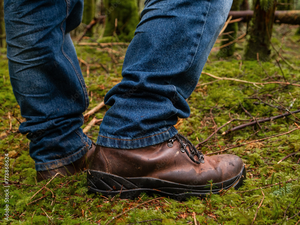 Tourist in blue jeans and tough brown leather outdoor boots on a green moss in a dense forest. Trip to nature and outdoor activity concept. Tourist in blue jeans and tough brown leather outdoor boots on a green moss in a dense forest. Trip to nature and outdoor activity concept.