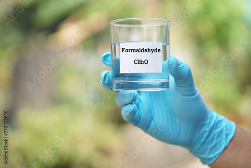 Foto Close up hand wear blue glove, holds test glass of Formaldehyde liquid with molecular formula CH2O
