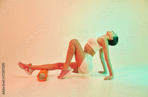 Using roller. Young fitness woman in sportive clothes against background in studio