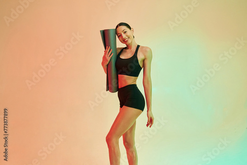 Time to practice, with yoga mat. Young fitness woman in sportive clothes against background in studio