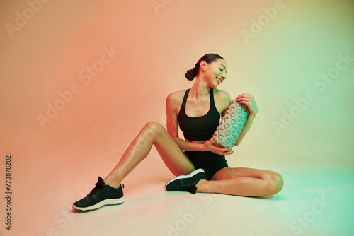 Beautiful young fitness woman in sportive clothes against background in studio with roller