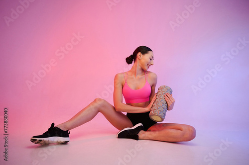 Wellbeing, with roller. Young fitness woman in sportive clothes against background in studio