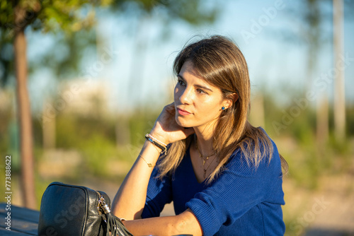 Relaxed and thoughtful woman sitting outdoors in a park.
