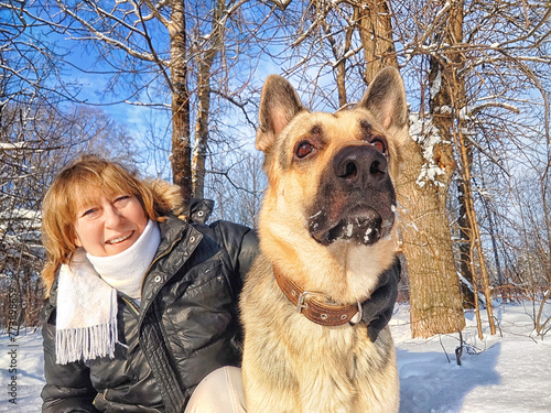 Adult girl or mature lady with shepherd dog taking selfies in winter nature landscape in a forest. Middle aged woman and big shepherd dog in cold day. Friendship, love, communication, fun, hugs