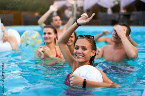 Fototapeta Naklejka Na Ścianę i Meble -  Friends have night pool party in a private villa swimming pool. Happy young people in swimwear splashing water, dancing with floaties and inflatable mattress, ball in a luxury resort.