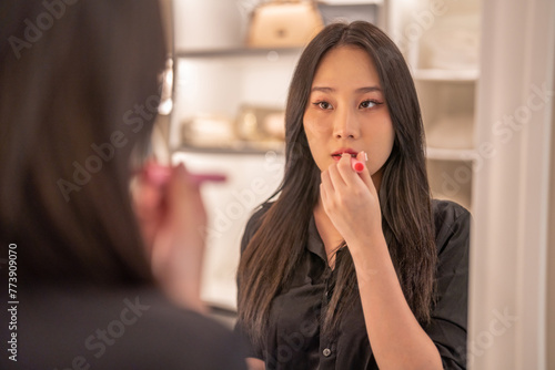 Smiling beautiful asian woman fresh healthy skin looking on mirror and enjoying applying skincare lips with red lipstick at home.facial beauty and cosmetic concept