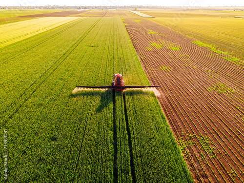 Drone shot of a tractor spraying in lush green wheat fields under the bright sun, showcasing modern agriculture © oticki