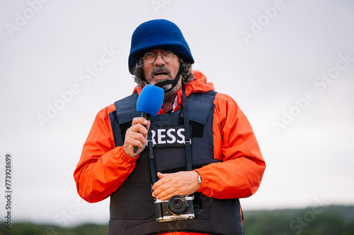 Press reporter in bulletproof vest holding a microphone.