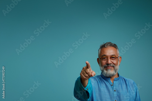 homme maghrébin pointant du doigt, avec les cheveux et la barbe grisonnants, portant des lunettes de vue et une chemise à col Mao, sur fond bleu dégradé avec espace négatif copy space. photo