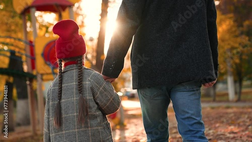 Little girl walks hand in hand with loving father through playground. Girl and father draw nearer to playground with interest. Girl and father go to playground to look at various play equipment photo