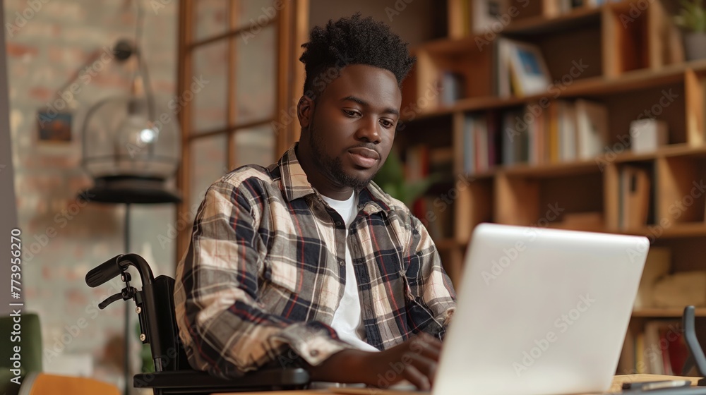 African American young man in a wheelchair at a desk looking at a laptop at home. Disabled person without the ability to move independently. Concept inclusivity at workplace, digital nomad 