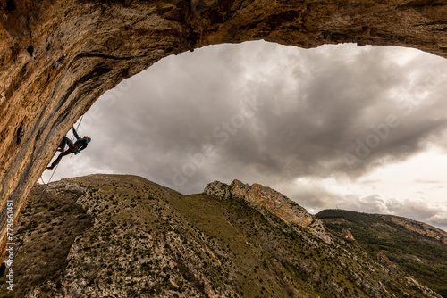 A man is climbing a rock face with a cloudy sky in the background. Scene is adventurous and daring