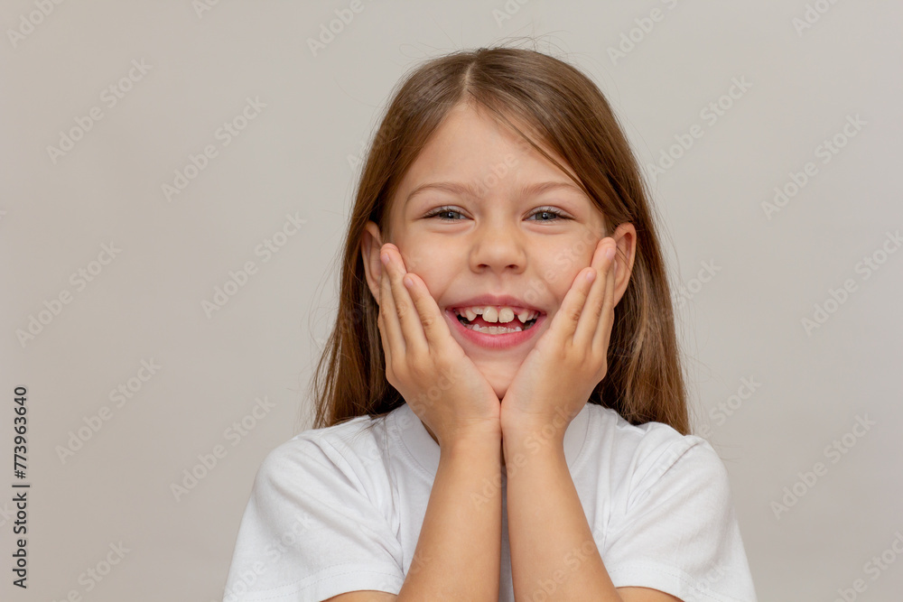 Portrait of caucasian little girl with open wide smile holding hands under chin looking at camera on white background Portrait of caucasian little girl with open wide smile holding hands under chin looking at camera on white background