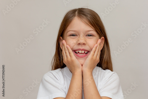 Portrait of caucasian little girl with open wide smile holding hands under chin looking at camera on white background