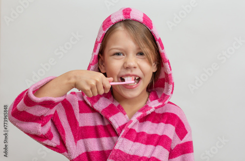 Portrait of caucasian little girl with open wide smile in bathrobe holding toothbrush close to teeth looking at camera on white background photo