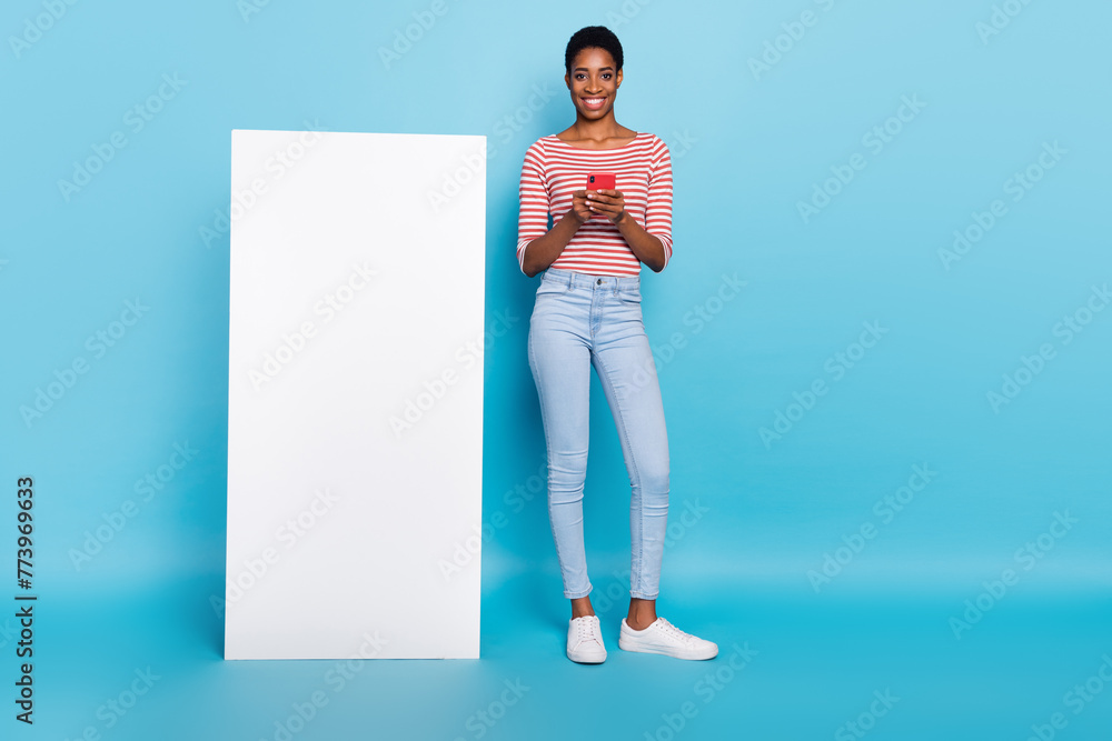 Photo of blogger lady hold telephone empty space vertical placard wear striped shirt isolated blue color background Photo of blogger lady hold telephone empty space vertical placard wear striped shirt isolated blue color background