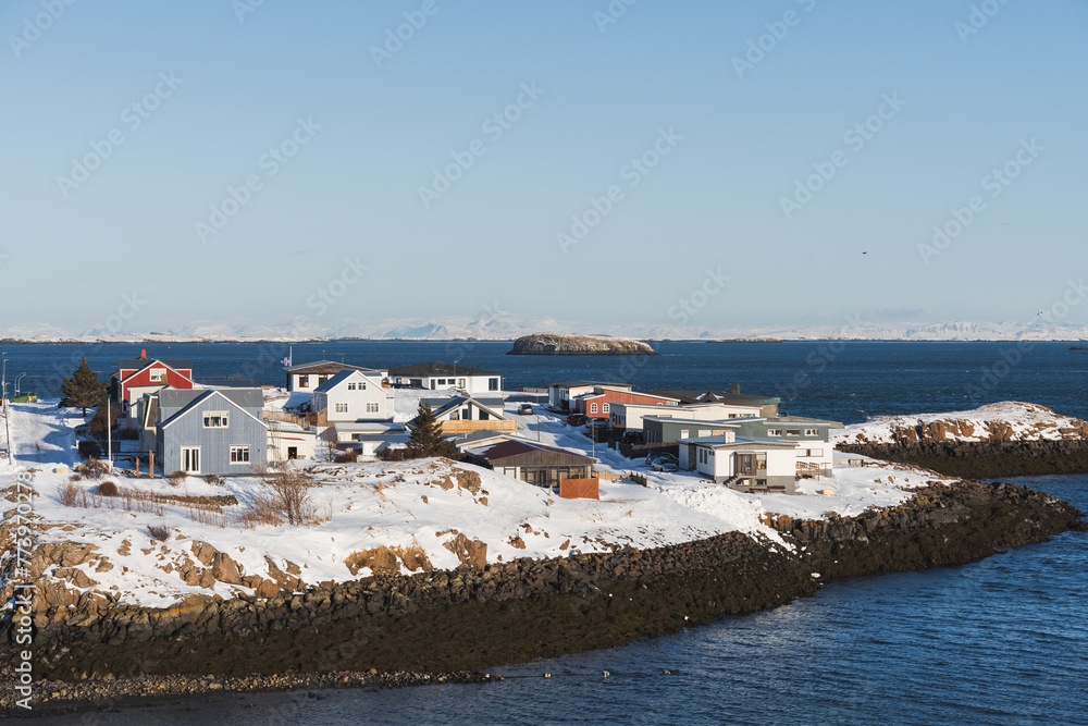 The quaint coastal architecture of an Icelandic town gleams under the winter sun, surrounded by a crisp sea and snow-dusted landscape The quaint coastal architecture of an Icelandic town gleams under the winter sun, surrounded by a crisp sea and snow-dusted landscape