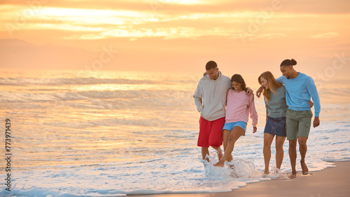 Hugging Couple With Friends In Casual Clothing On Vacation Walking Along Beach Shoreline At Dawn