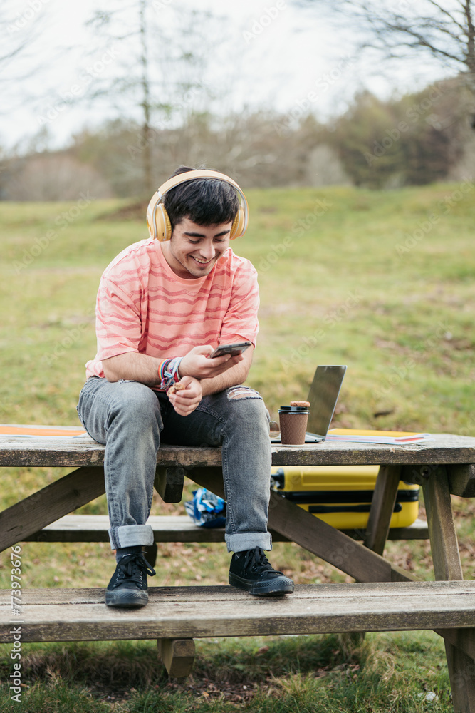 A relaxed man enjoys his music, sitting with a laptop and coffee at a rustic outdoor table, immersed in nature A relaxed man enjoys his music, sitting with a laptop and coffee at a rustic outdoor table, immersed in nature