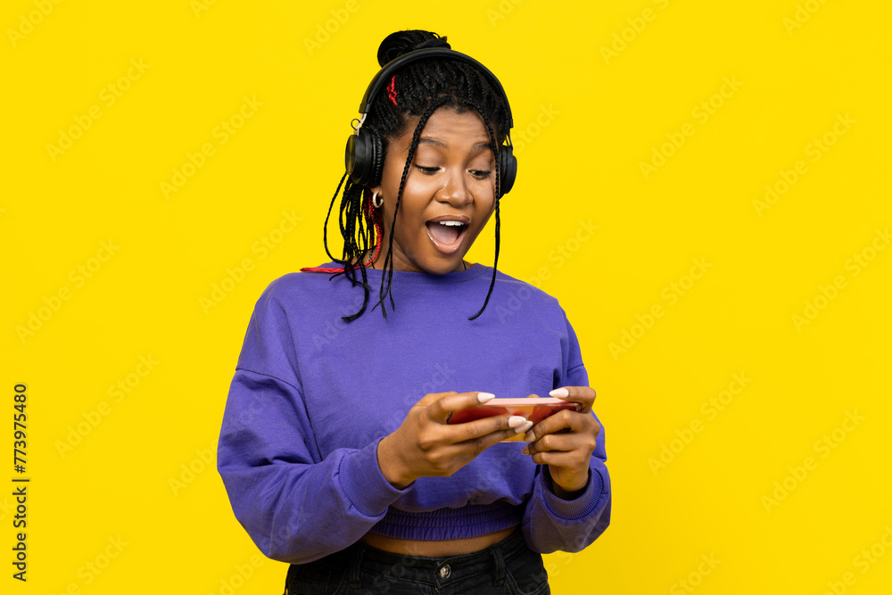 Woman suprised and immersed in music, using their smartphone with headphones on a bright yellow background. Woman suprised and immersed in music, using their smartphone with headphones on a bright yellow background.