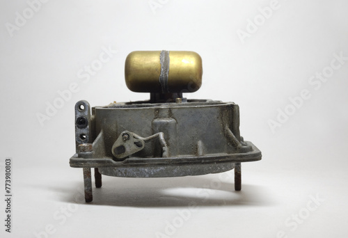 old obsolete carburetor. air intake horns body with attached float, blurred. standing Upside down on threaded rods, on dusty background photo