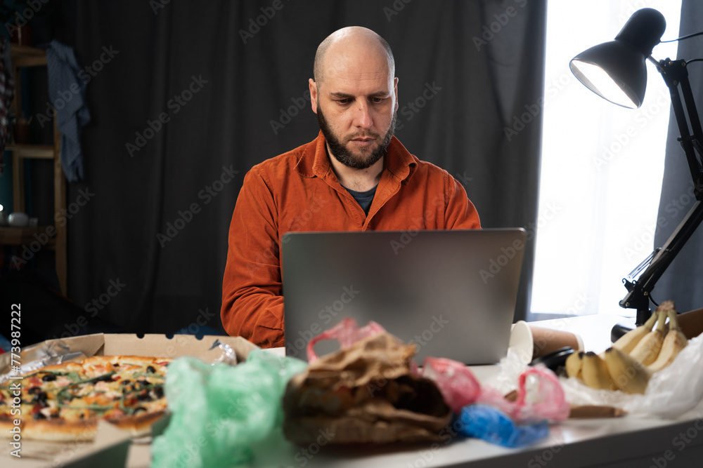 Portrait of focused man using laptop, typing on keyboard, chatting, working at home. Successful freelancer working online sitting in messy room Portrait of focused man using laptop, typing on keyboard, chatting, working at home. Successful freelancer working online sitting in messy room