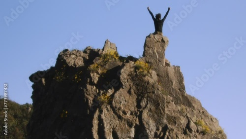 A climber stands victorious on the rugged peak, arms raised in jubilation against a clear sky. This cinematic shot, taken with a high-quality Blackmagic camera, freezes the moment of triumph photo