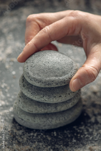 Natural soap in the shape of stones stacked on top of each other on a black background covered with sea salt and a hand puts the top stone. Concept of organic cosmetics and spa