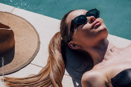 Beauty fashion model girl lying near pool and relaxing, sunbathing. Beautiful young woman portrait over pool background, sun tan concept. Vacation © Subbotina Anna
