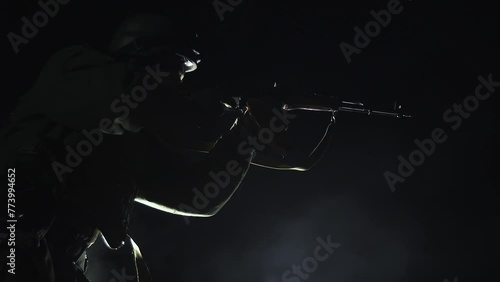 SLOW MOTION - Silhouette of military soldier, infantryman with weapons at night. Warrior shoots, holding machine gun, darkness, night background. Flash from a shot from a firearm on a black background