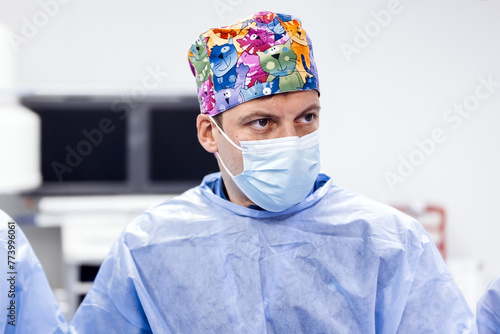 Experienced surgeons in medical gowns, caps, masks and gloves perform an operation in a modern clinic. Group of professional doctors using modern medical equipment in operating room.