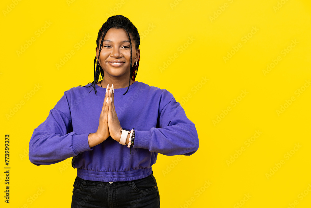 An afro woman making gesture of gratitude or asking for forgiveness smiling confident in purple sweater on yellow background. - obrazy, fototapety, plakaty 