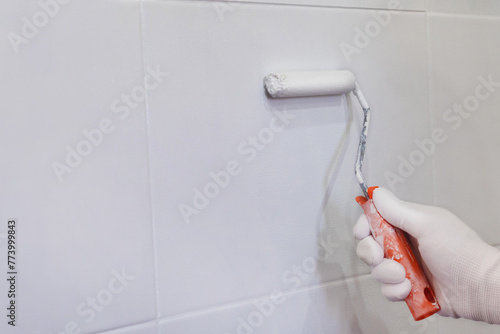 Painting tiles in the kitchen in the bathroom, white paint with a roller. Hand in glove with roller © Katyart