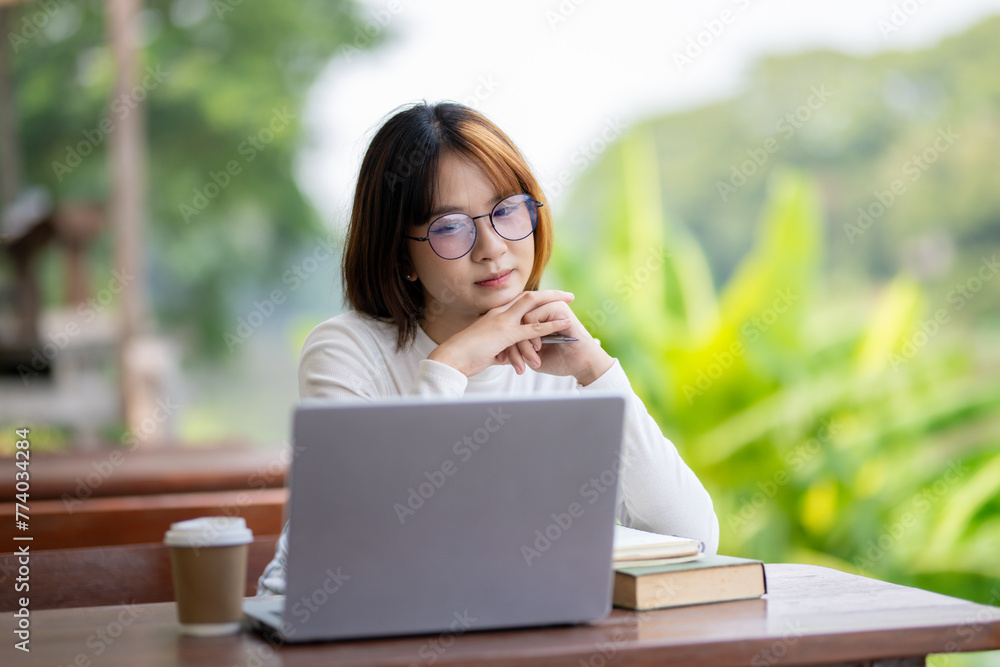 Young woman wearing glasses sitting at a garden table, looking thoughtful with a laptop and notebooks in front of her.
Young woman wearing glasses sitting at a garden table, looking thoughtful with a laptop and notebooks in front of her.