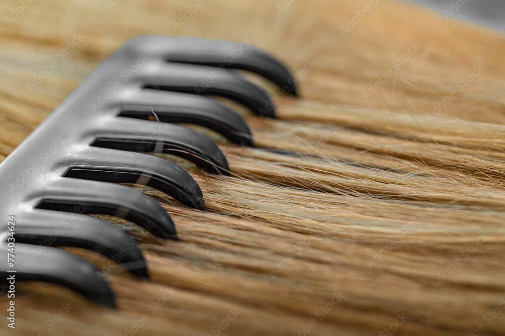 Obraz premium Czesać włosy, zbliżenie na grzebien w kosmykach blond wlosow