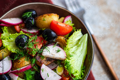 A close-up of a delicious Mediterranean salad bowl, with golden potatoes, ripe cherry tomatoes, black olives, spring onions, radishes, and lettuce, tastefully garnished with dill photo