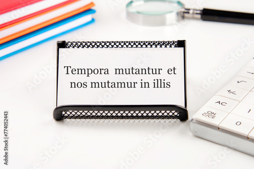Tempora mutantur et nos mutamur in illis Translated from Latin, it means Times are changing, and we are changing with them. on a white business card on a table with office supplies photo